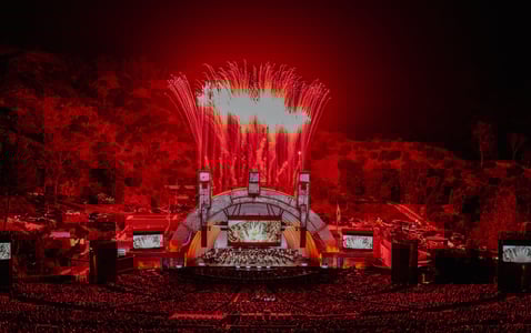 Fireworks go off at an outdoor concert venue where a Marvel movie is screened behind an orchestra. 